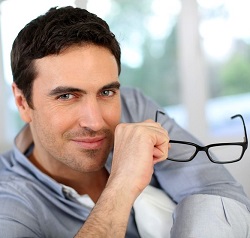 Man in a couch wearing pastel long sleeves and holding his eyeglasses